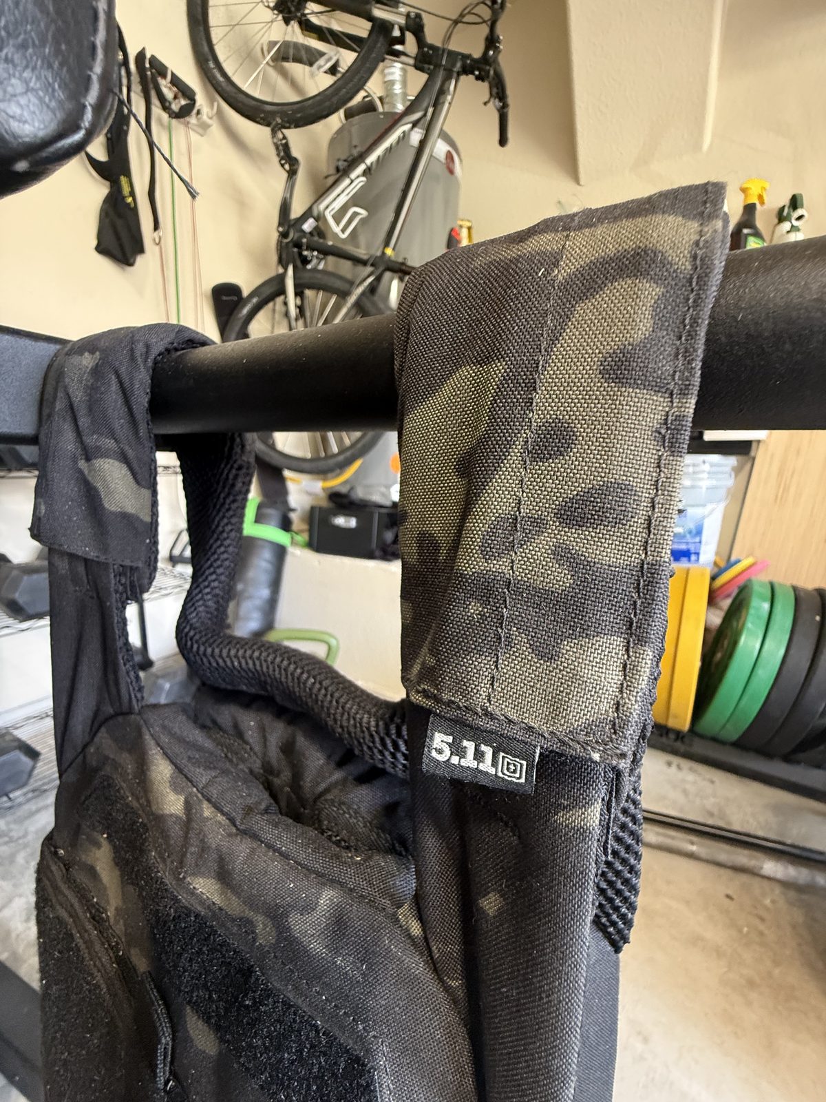 The 5.11 TacTec Trainer in MultiCam Black hanging in the gym next to the dumbbell rack